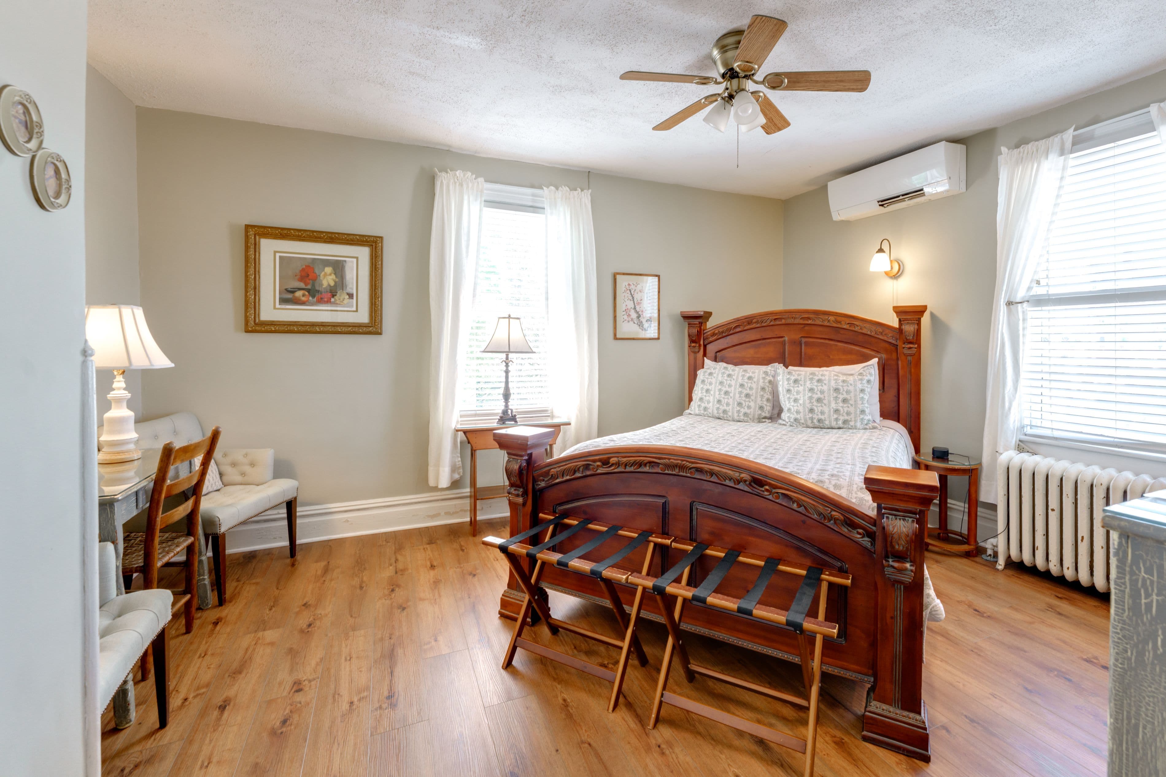 Room features wood floors, a queen bed, and sitting area with two cushioned chairs and painted desk.