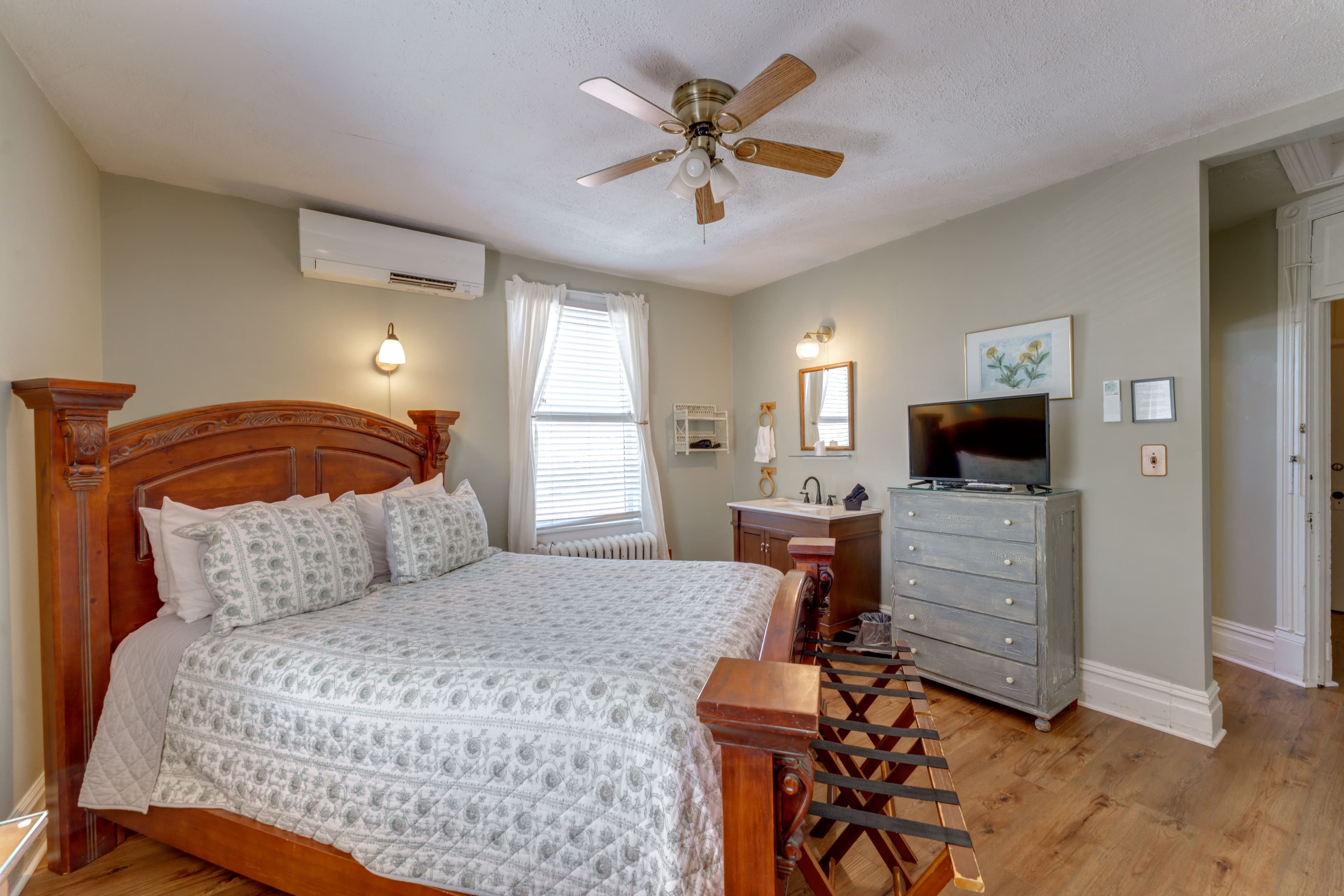 Room features queen bed, in room vanity and tall dresser with a TV on top.