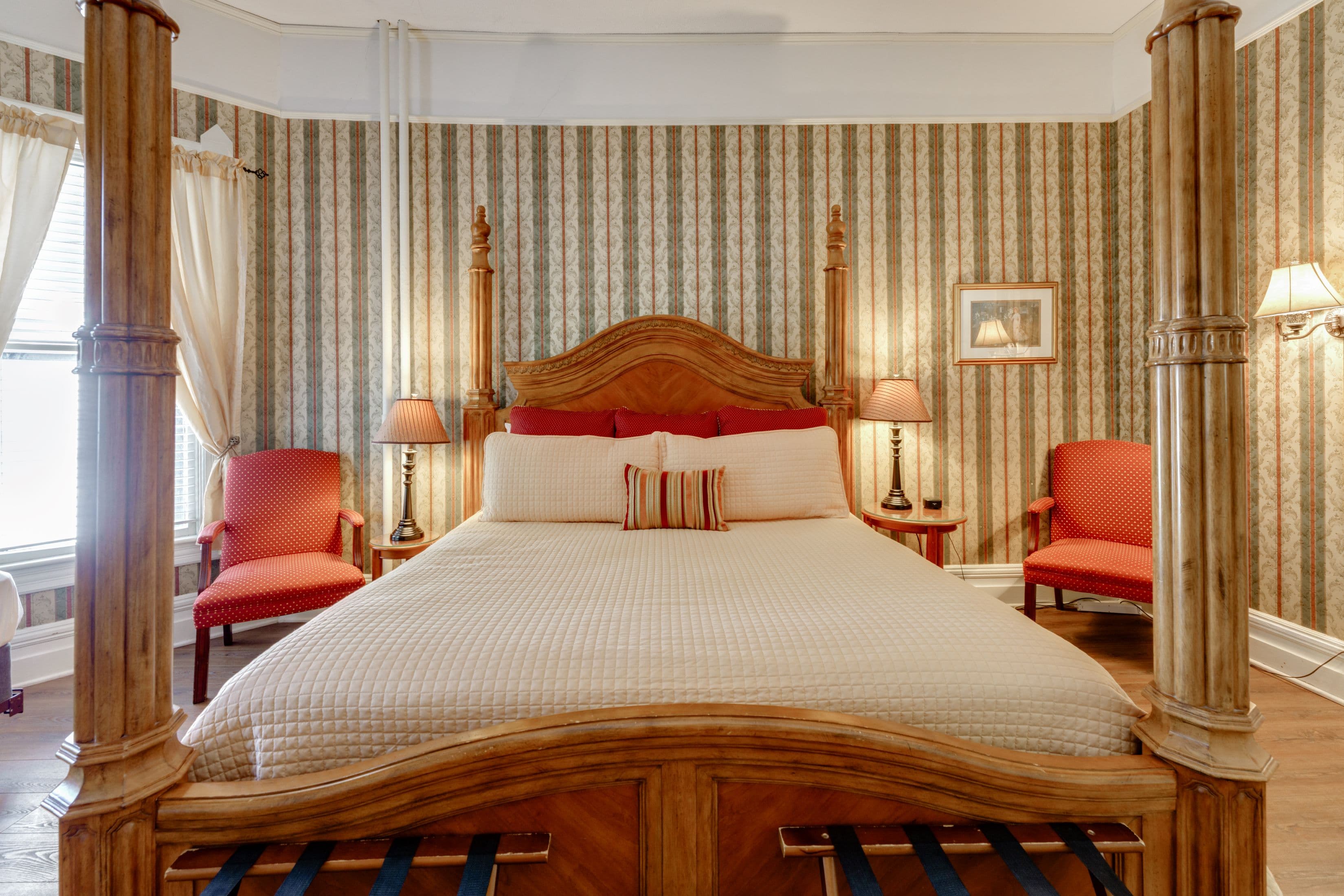 Room features four posted king bed with a night stand and cushioned chair on both sides.
