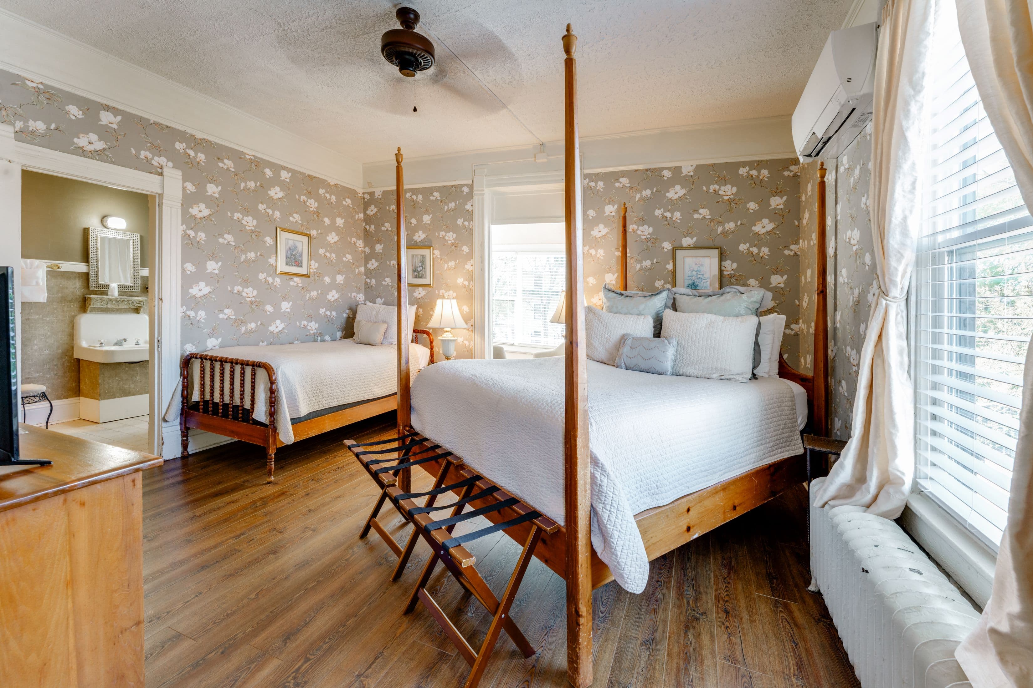 Room features wood flooring, floral wallpaper, four posted queen bed, and twin bed.