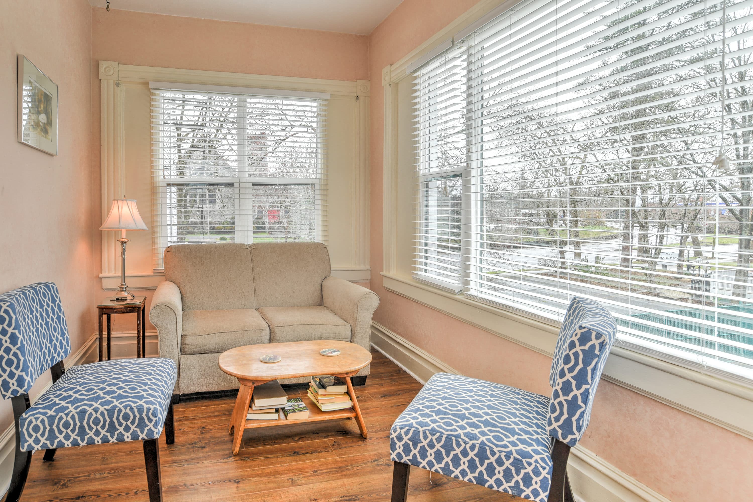 Sitting room features large windows, pull-out couch, two cushioned chairs, and wooden coffee table.