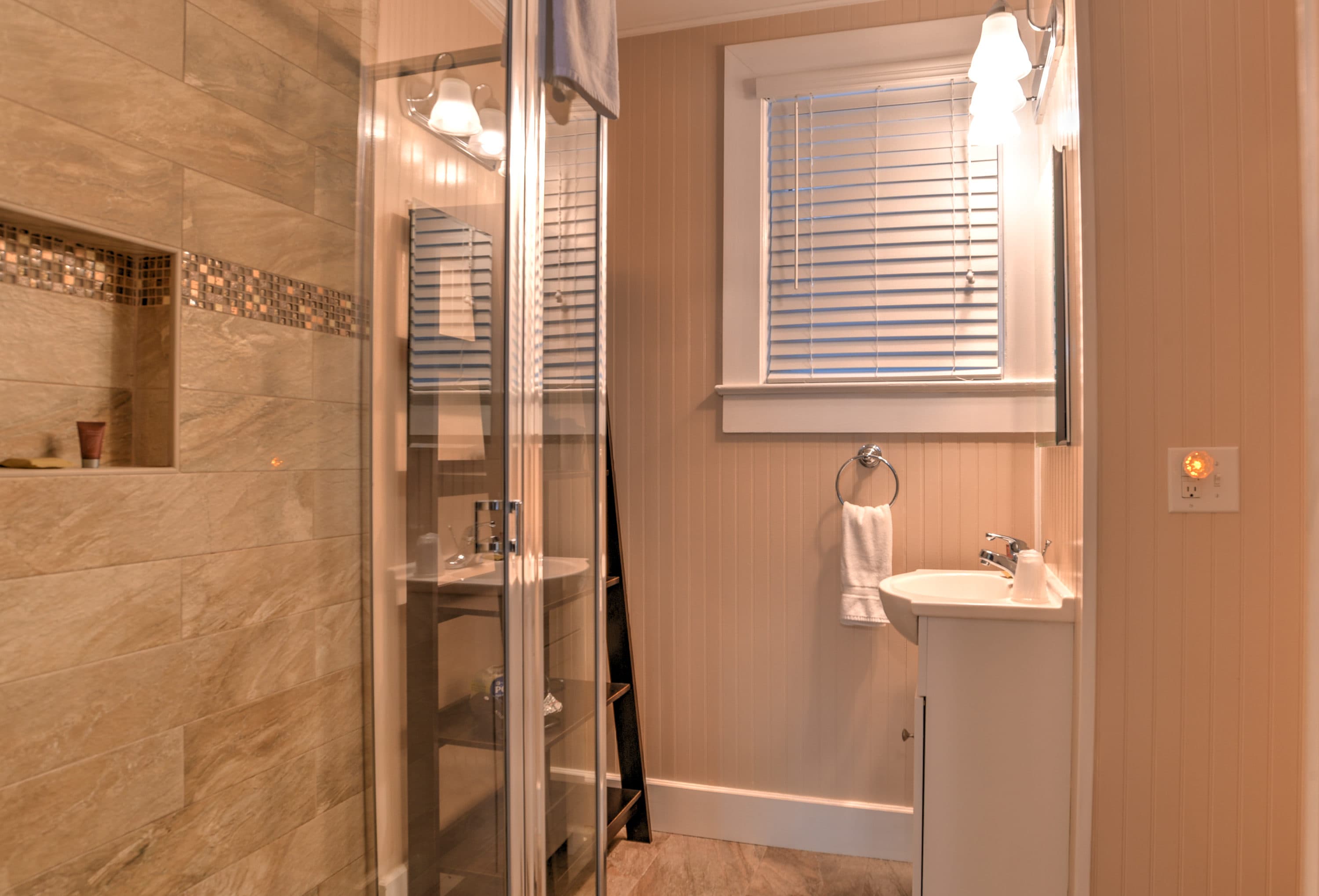 A modern bathroom featuring a glass shower, sink with a mirror, and natural light from a window.