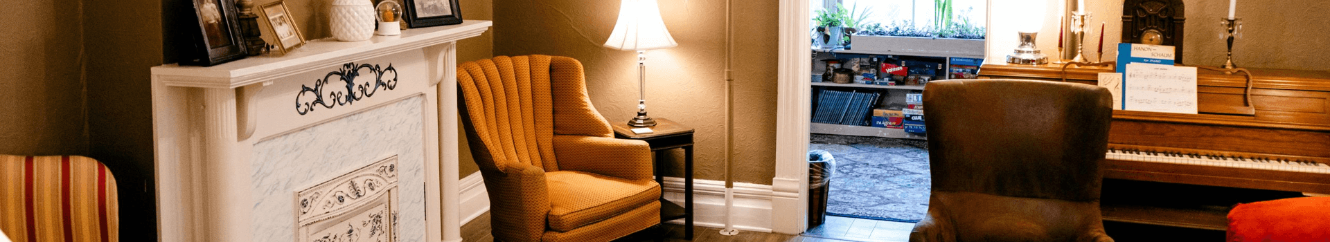 A cozy living room featuring an orange armchair, a piano, and a bright doorway leading to another room.