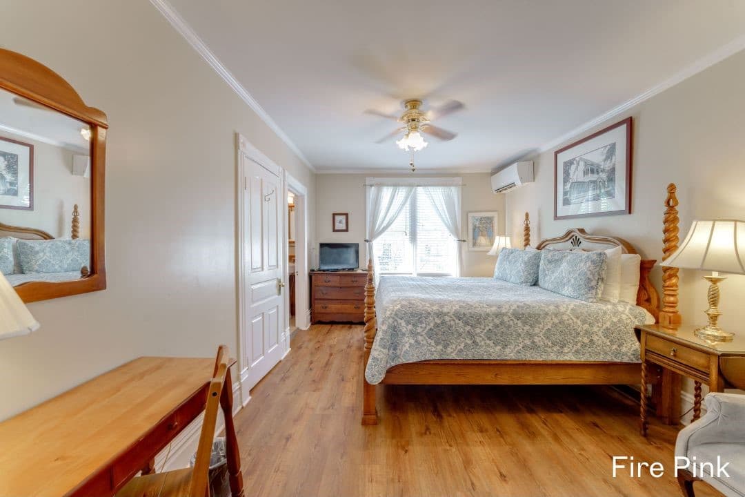 Fire Pink room features a king bed, a night stand and lamp on each side, a dresser with a TV on top, and a desk and chair.