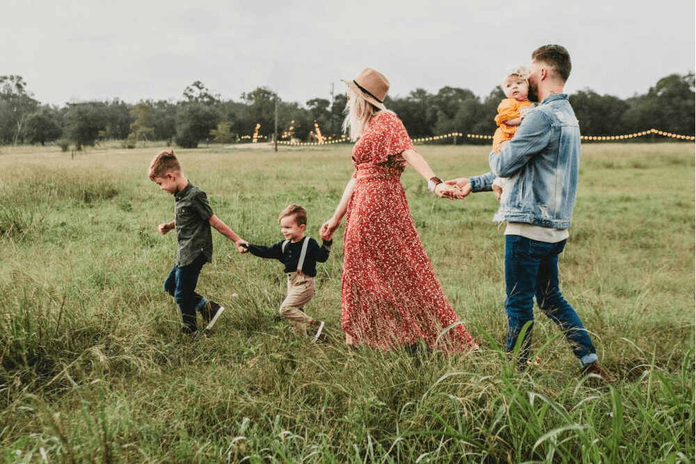 A family of four walks hand-in-hand through a grassy field.