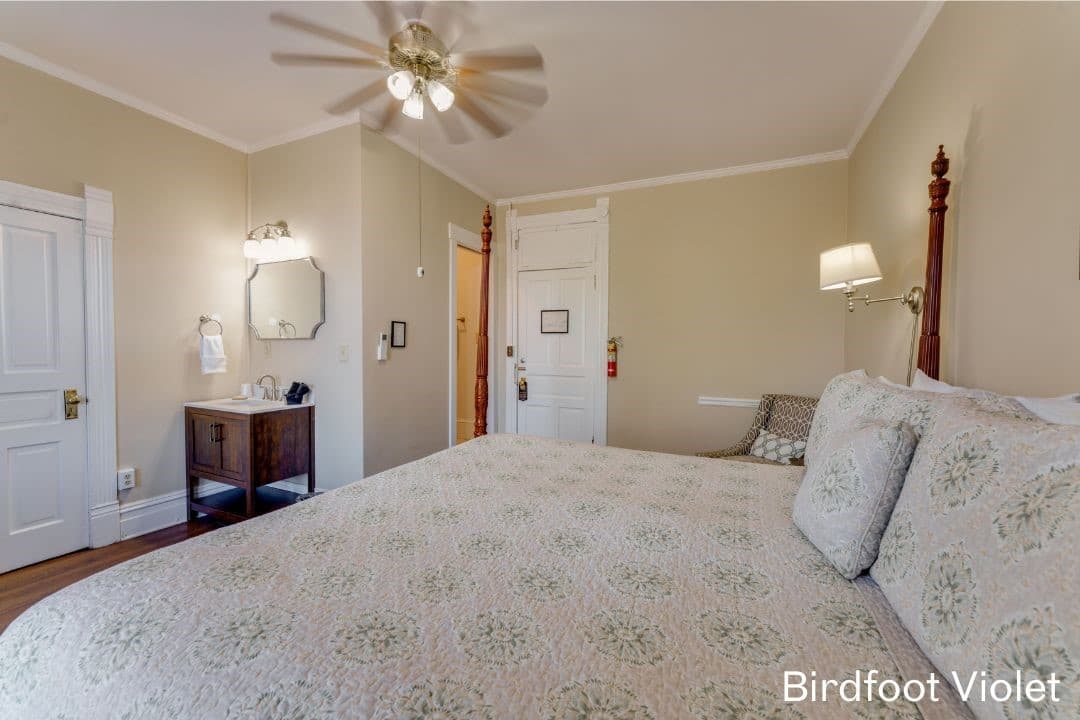 Birdfoot Violet Room features a four-posted king bed, an in-room vanity and sink, and a cushioned chair in the corner.