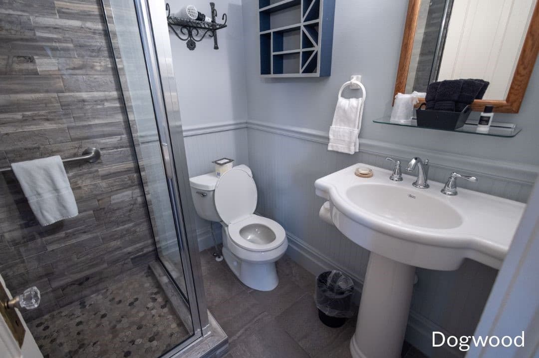 Dogwood's bathroomfeaturing a large, tiled walk-in shower, white pedestal sink, and white toilet.