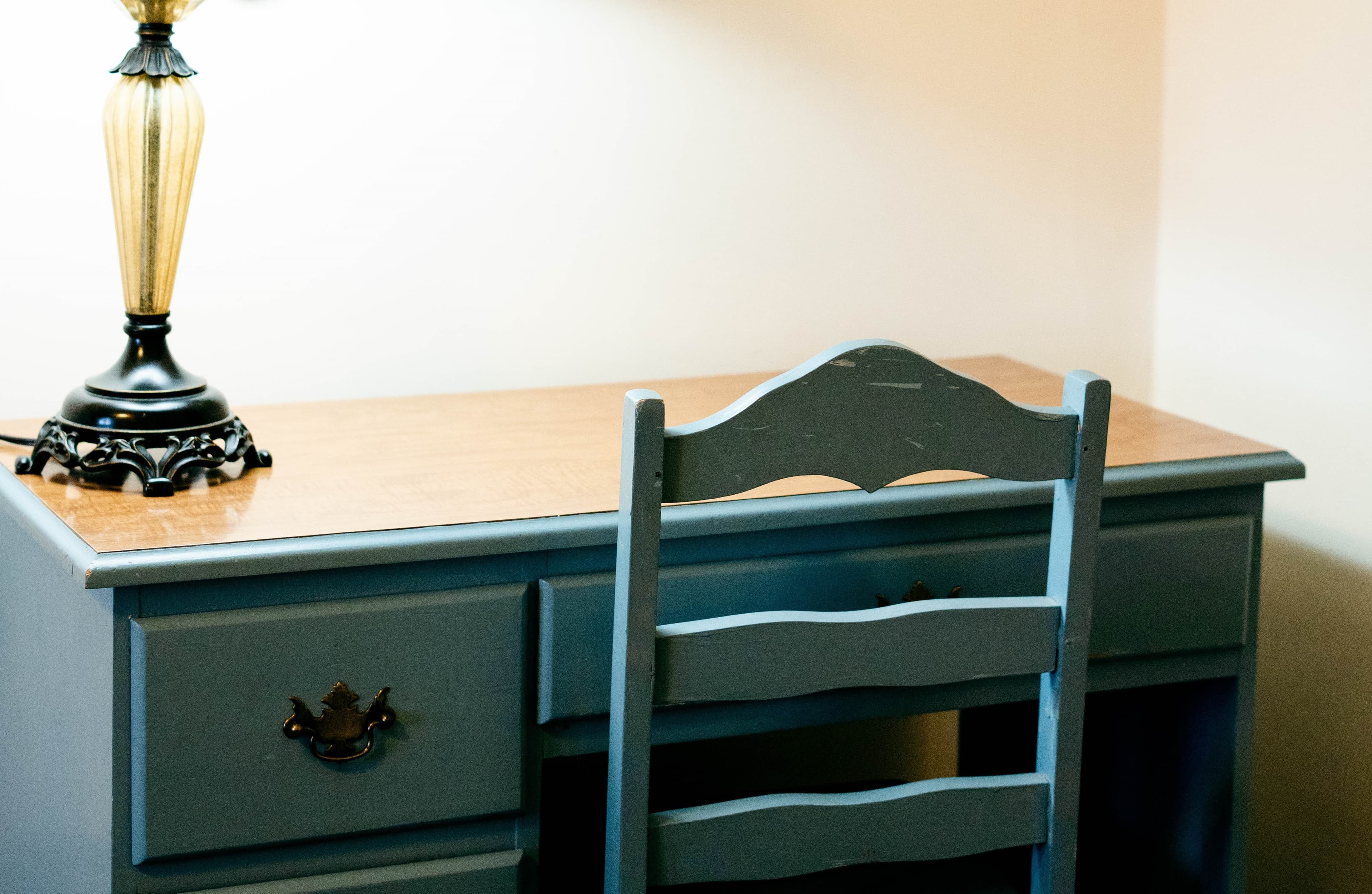 A wooden desk with a light-colored top and a blue chair, accompanied by a decorative lamp.