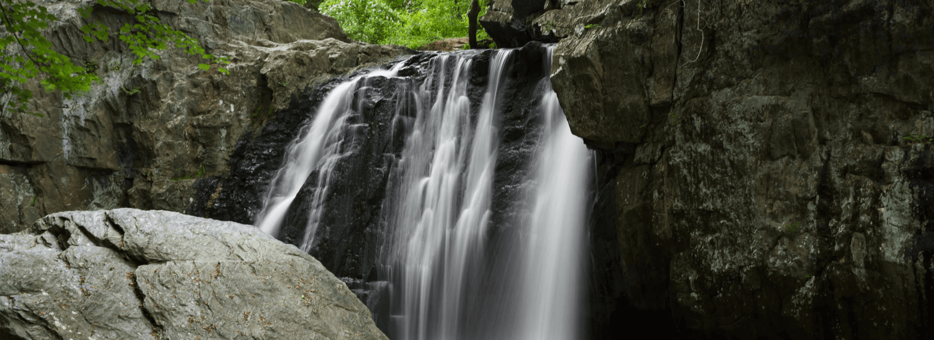 A tranquil waterfall cascading over rocky cliffs surrounded by lush green foliage.