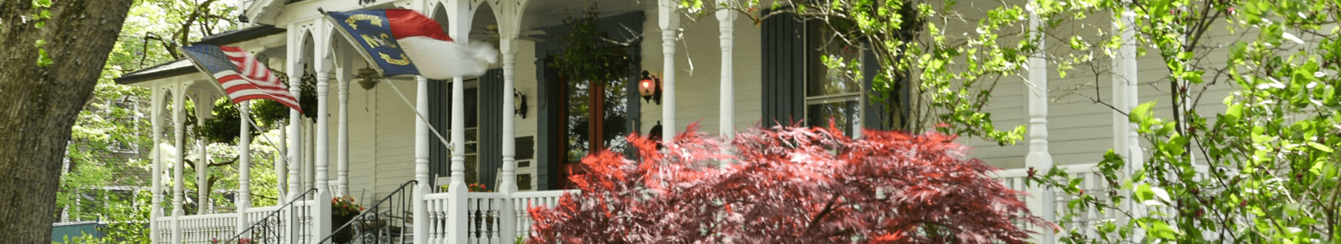 A cozy house with a front porch, featuring American and North Carolina flags and vibrant greenery.