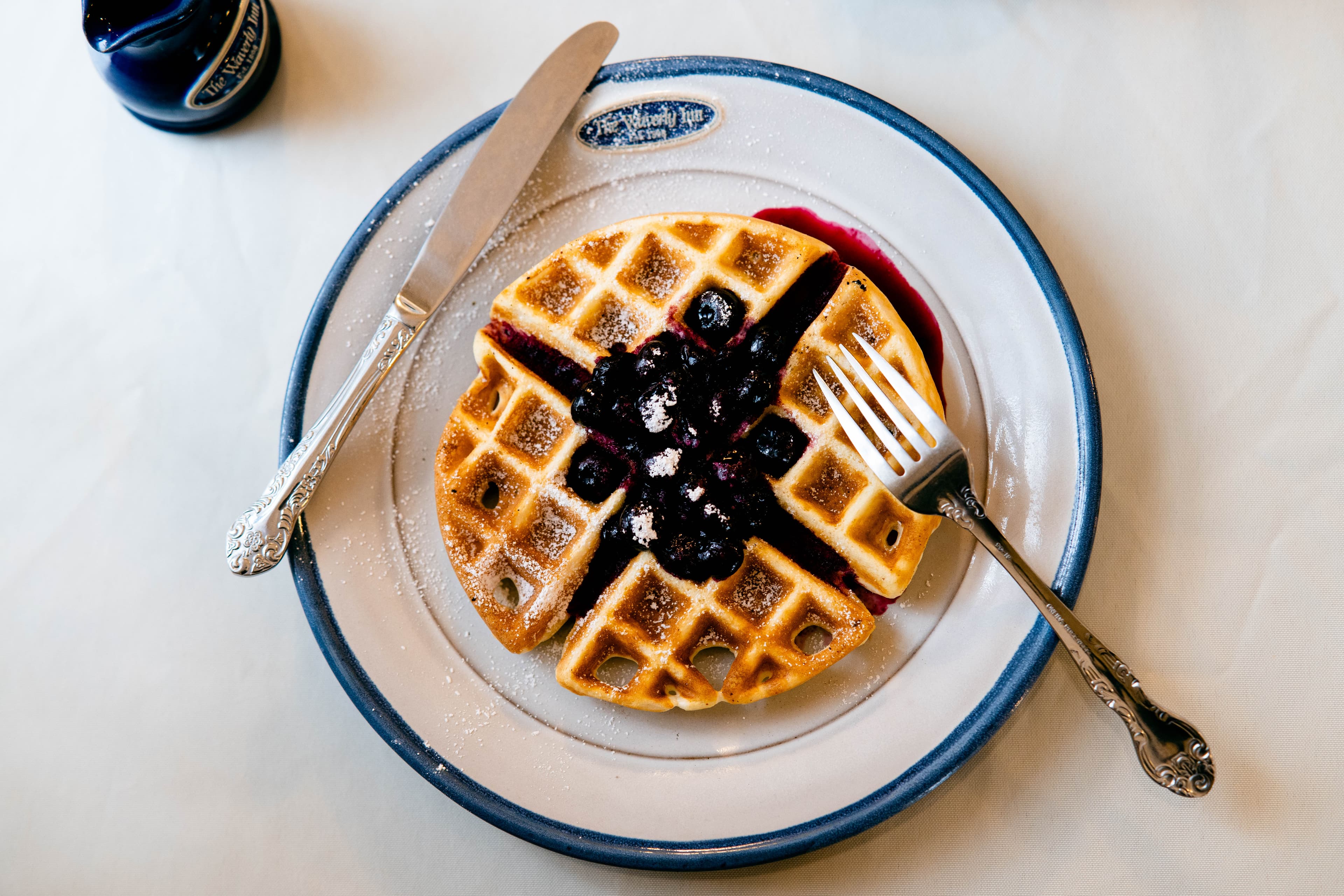 A plate of waffles topped with blueberry sauce and powdered sugar, accompanied by a knife and fork.