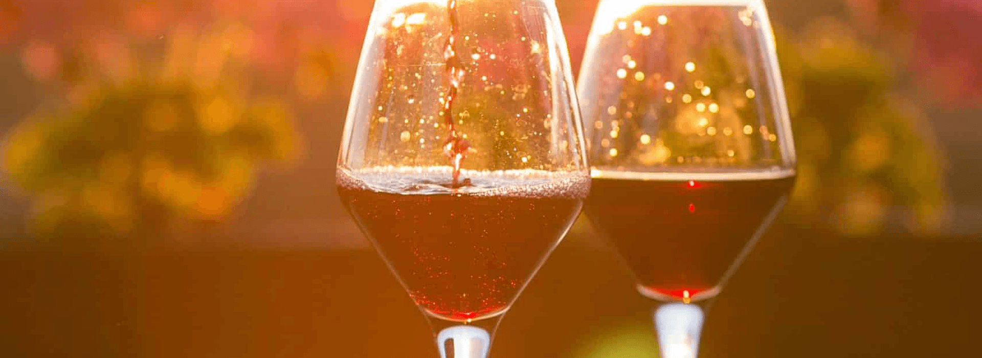 Two glasses of red wine sparkle in warm sunlight.