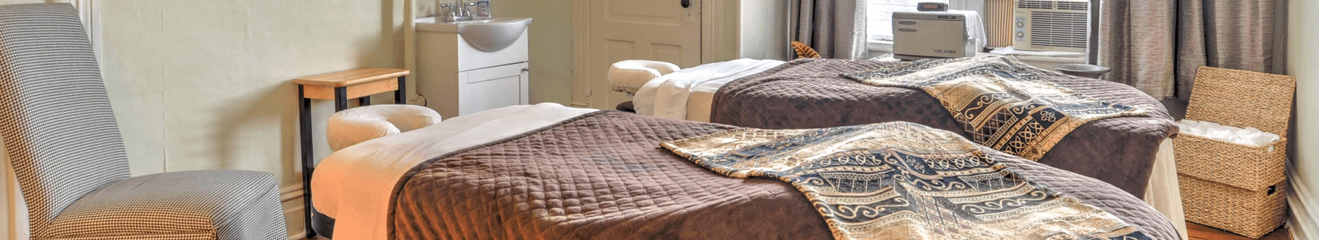 A tranquil massage room featuring two treatment tables and a comfortable chair.
