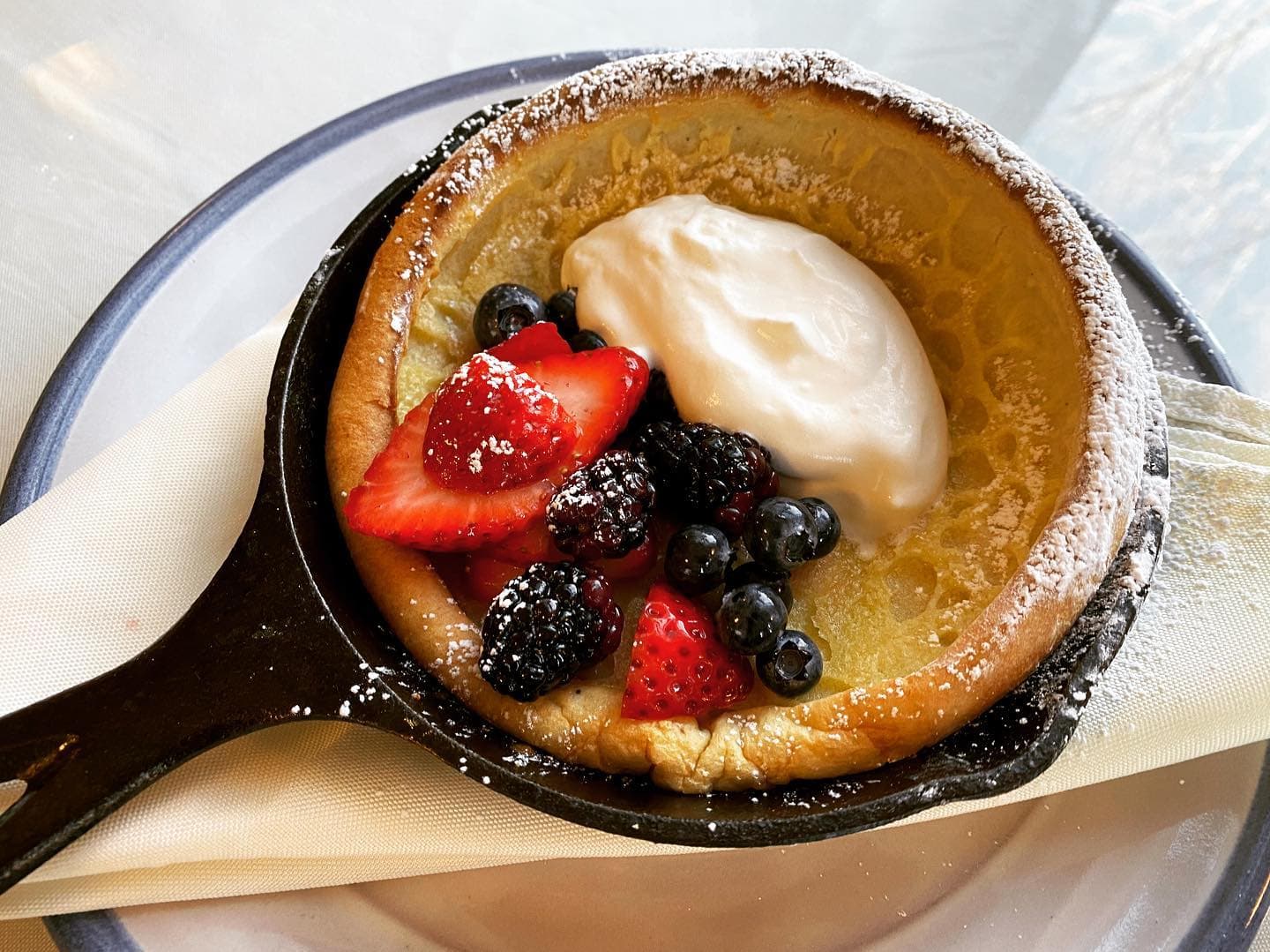 A baked Dutch baby pancake topped with fresh berries and whipped cream, served in a skillet.