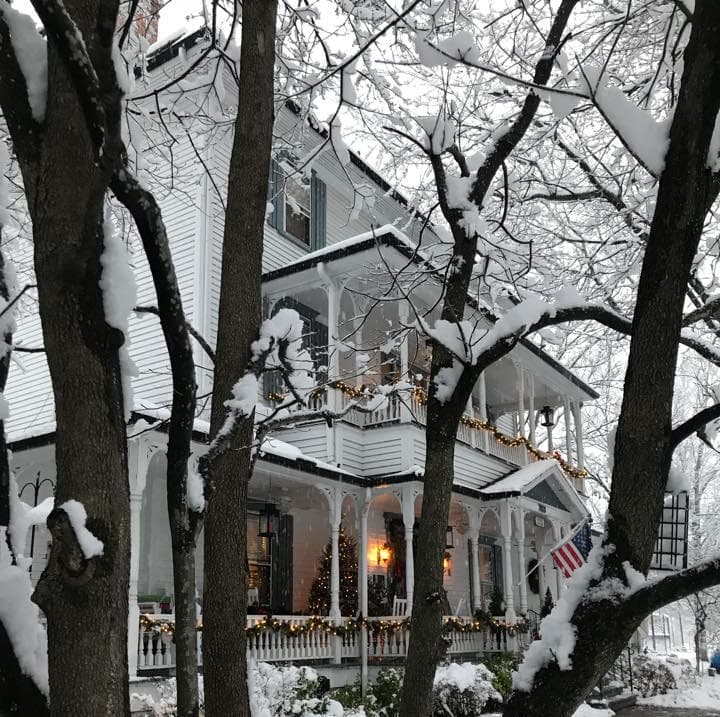 A snowy white Victorian house decorated for the holidays, framed by bare trees. A snowy white Victorian house decorated for the holidays, framed by bare trees.