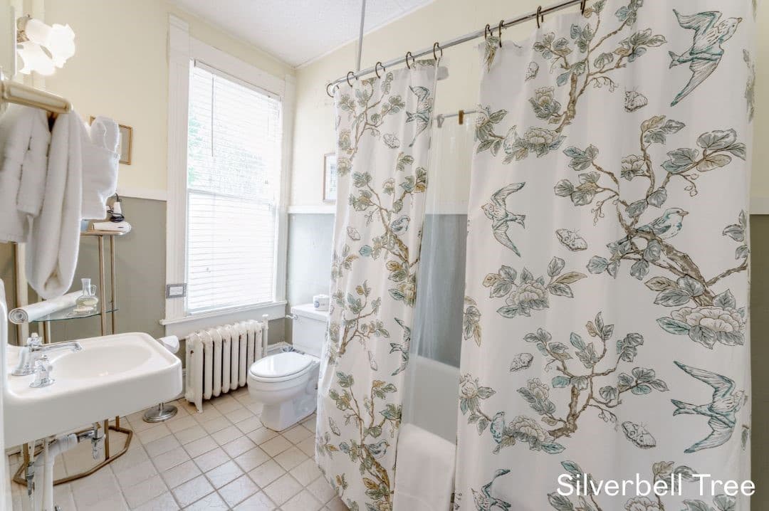 Silverbell Tree's bathroom features a large claw footed tub with a wrap around shower curtain, a white sink and toilet, and towel racks.
