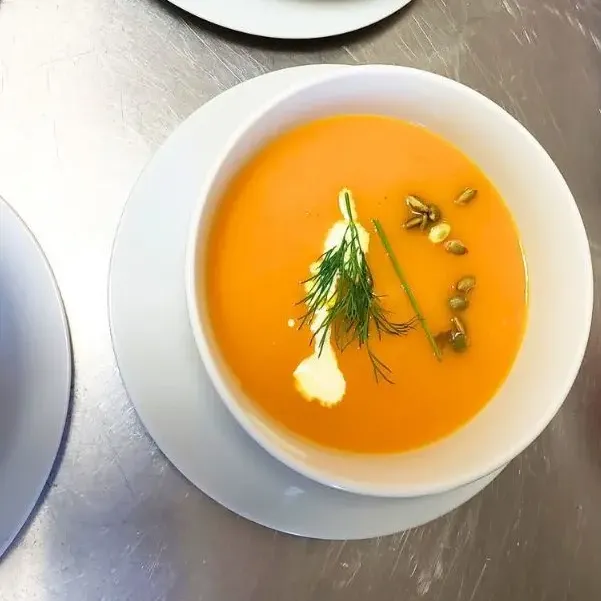 A creamy orange soup garnished with herbs and seeds in a white bowl.
