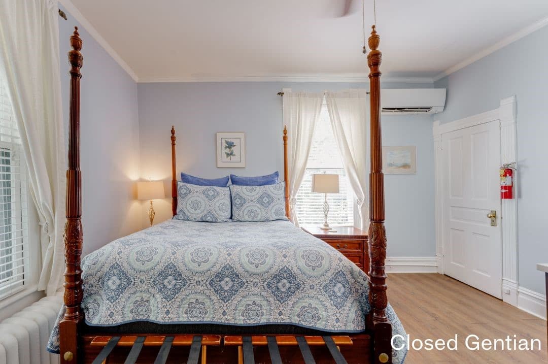 Closed Gentian Room featuring a four-posted queen bed, luggage racks, and a night stand on each side.