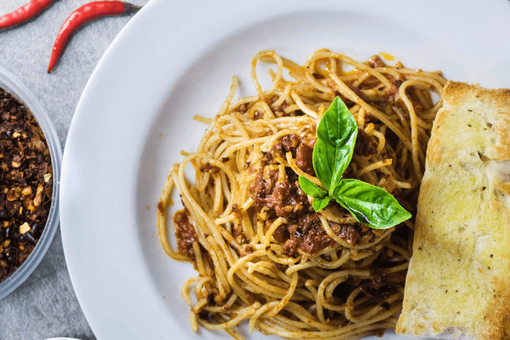 A plate of spaghetti with marinara sauce and a slice of garlic bread, garnished with fresh basil.