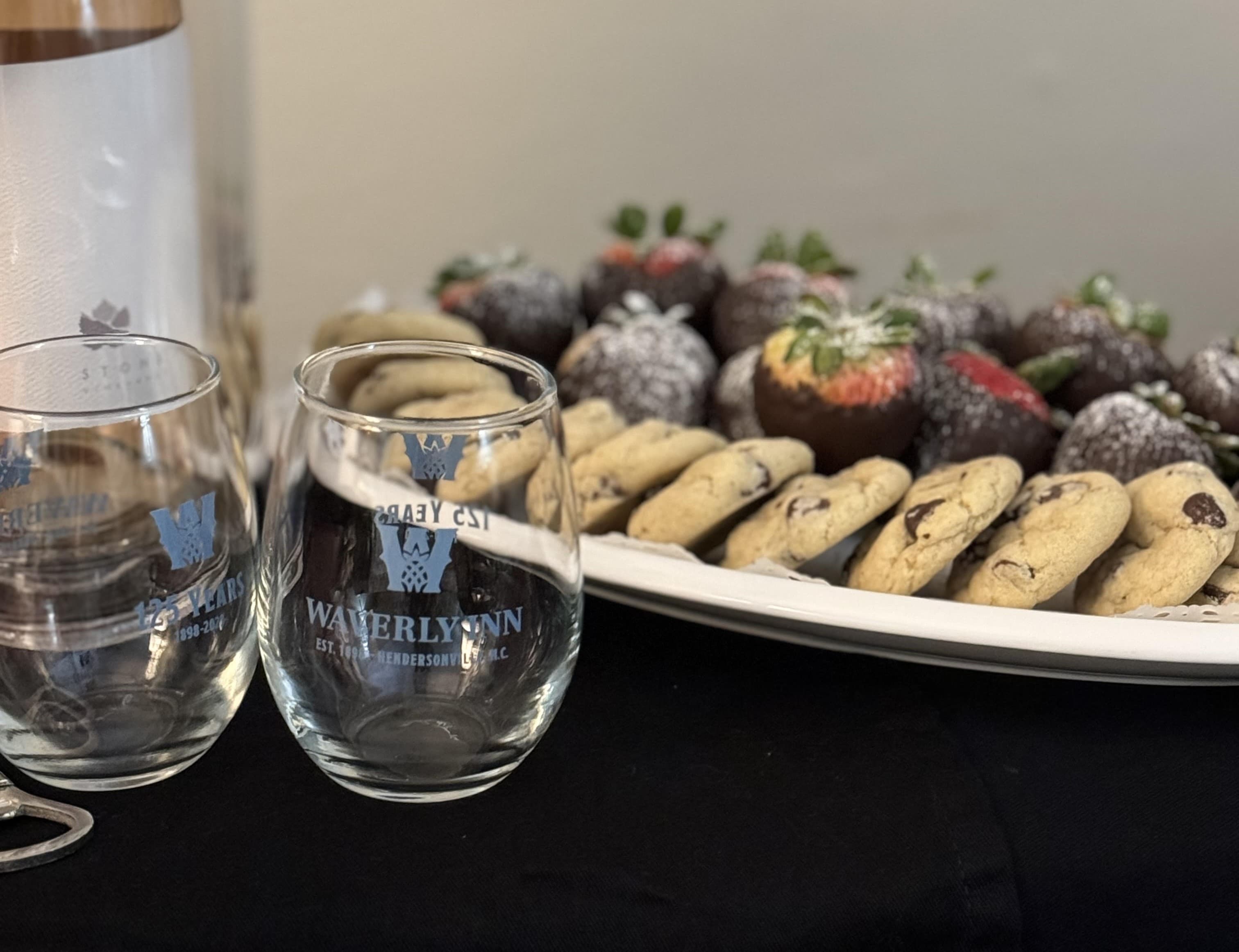 Two etched glassware pieces next to a platter of cookies and chocolate-covered strawberries.