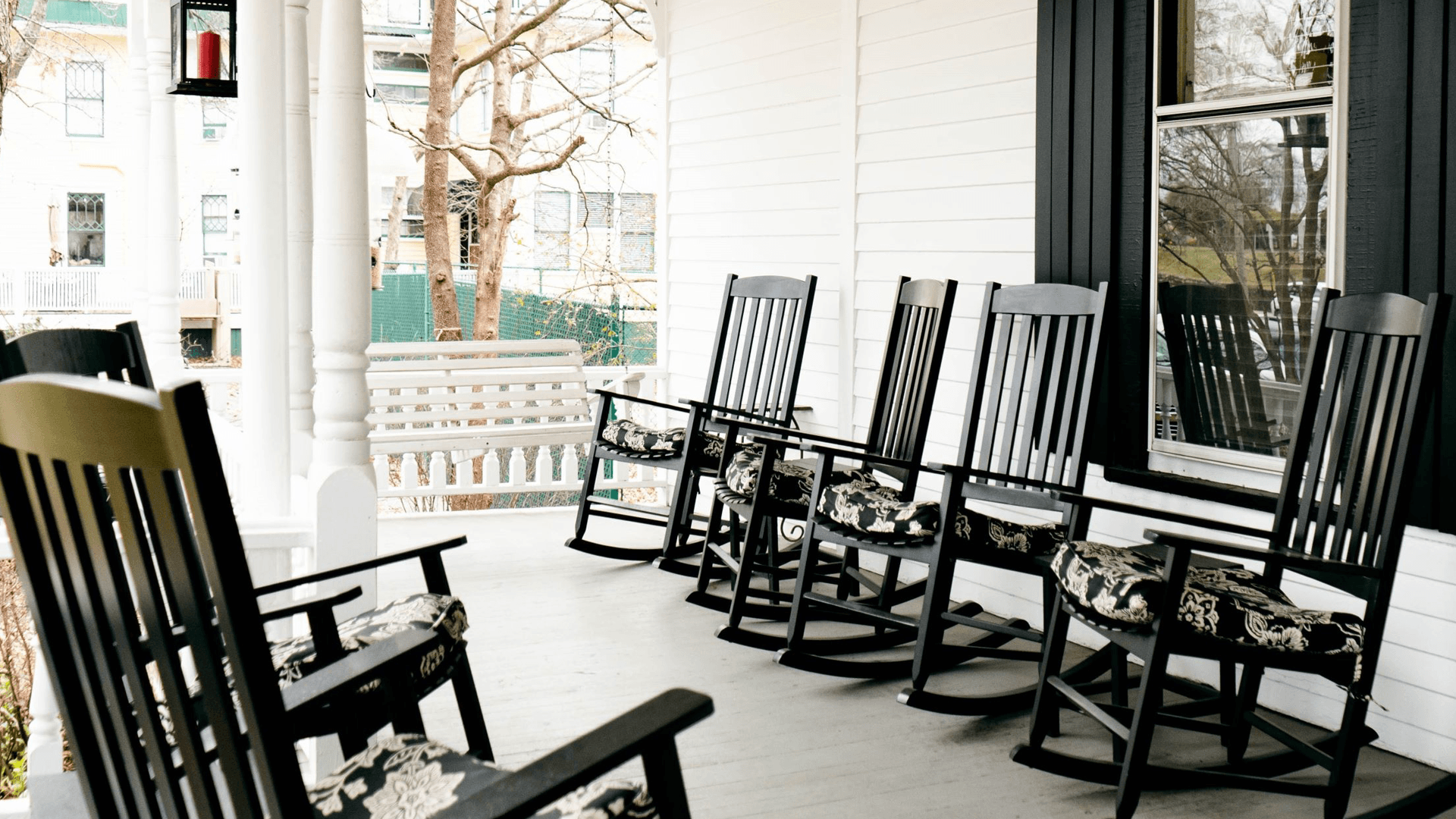 A porch with several black rocking chairs and a swing, set against a white backdrop.