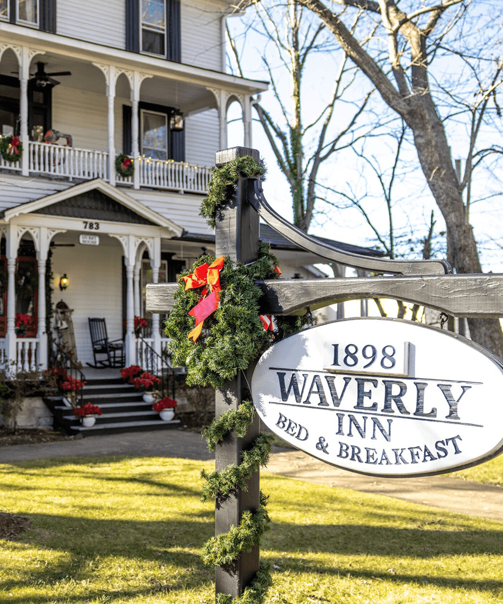 Sign for Waverly Inn, a bed and breakfast established in 1898, with festive decorations in front of a historic house.