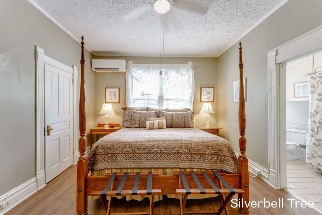Silverbell Tree room features a four posted king bed with a night stand and lamp on each side, and lugage racks at the bottom.