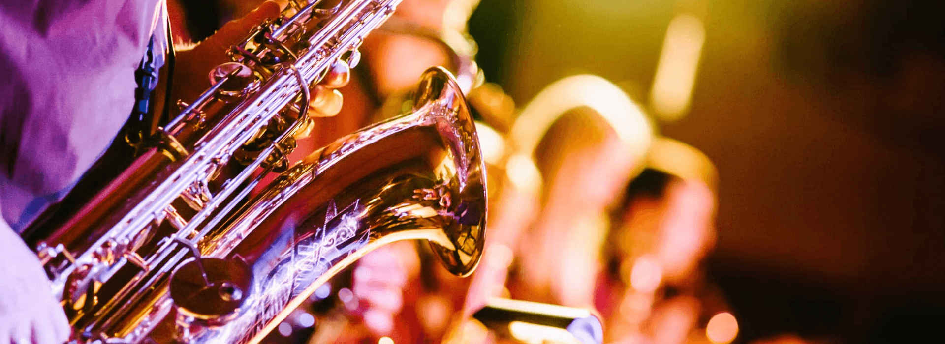 A close-up of a saxophone being played on stage, with colorful lights in the background.