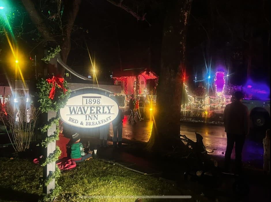 A lit sign for the Waverly Inn Bed & Breakfast amidst a festive nighttime scene.