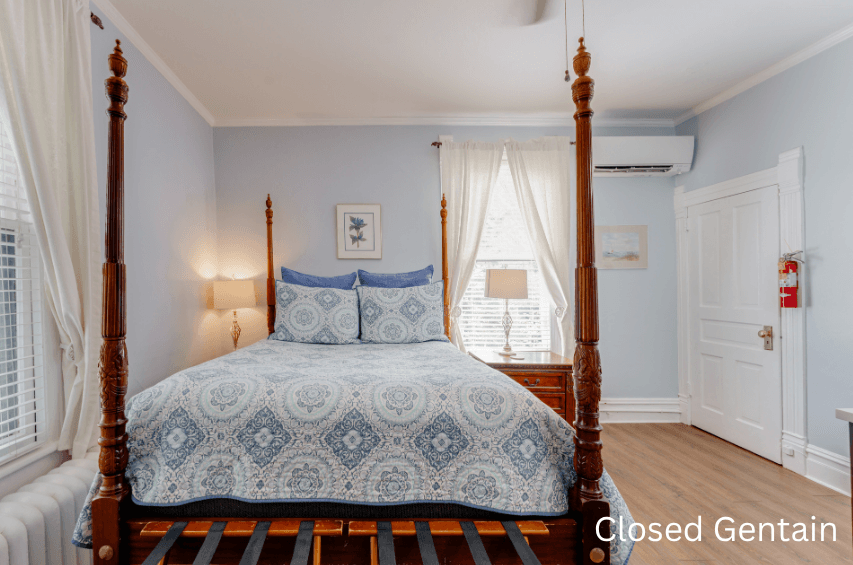 A cozy bedroom featuring a four-poster bed with blue and white patterned bedding, soft lighting, and natural light coming through the windows.