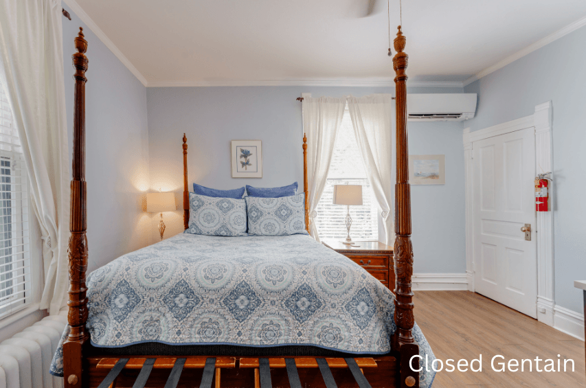 A cozy bedroom featuring a four-poster bed with blue and white patterned bedding, soft lighting, and natural light coming through the windows.
