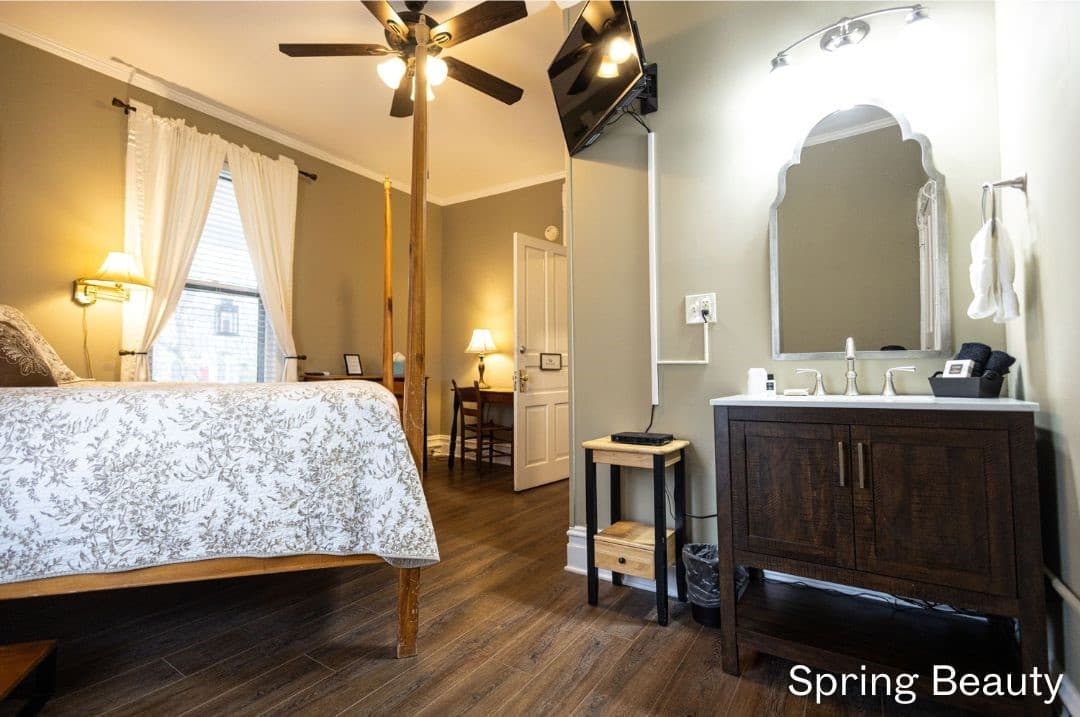 Spring Beauty Room featuring an in-room sink and vanityand four posted queen bed. A desk and chair and short dresser are in the oposite corner.