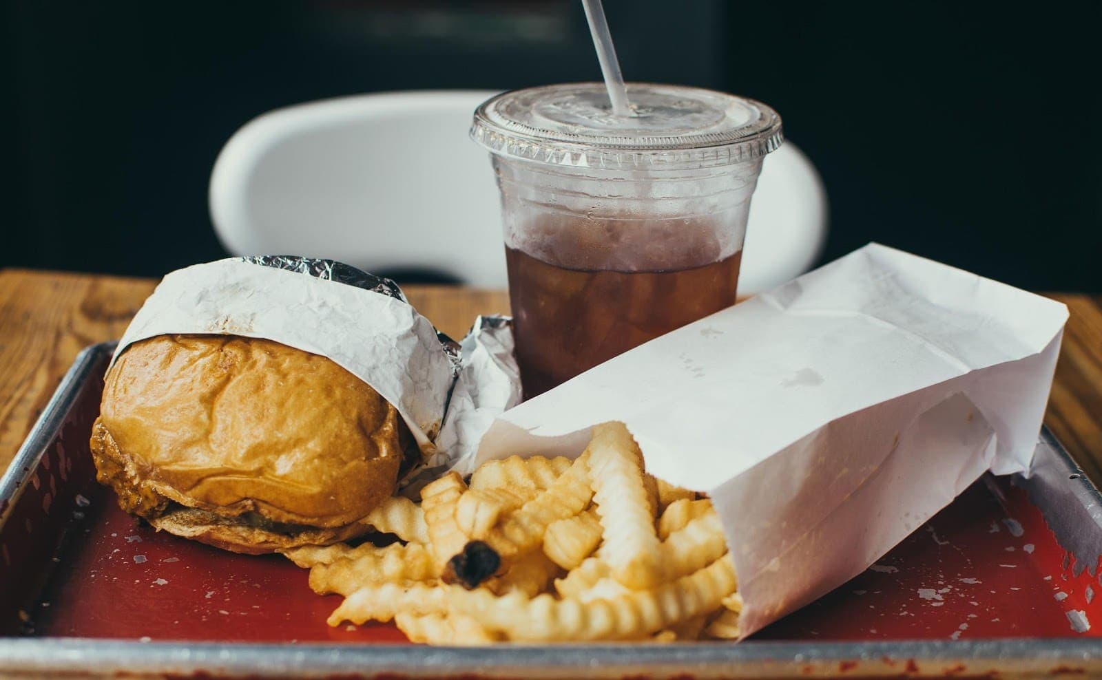 A wrapped burger, crinkle-cut fries, and iced tea on a metal tray. A wrapped burger, crinkle-cut fries, and iced tea on a metal tray.