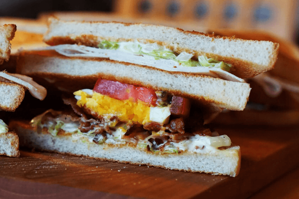 A close-up of a layered sandwich with bacon, lettuce, tomato, and egg.