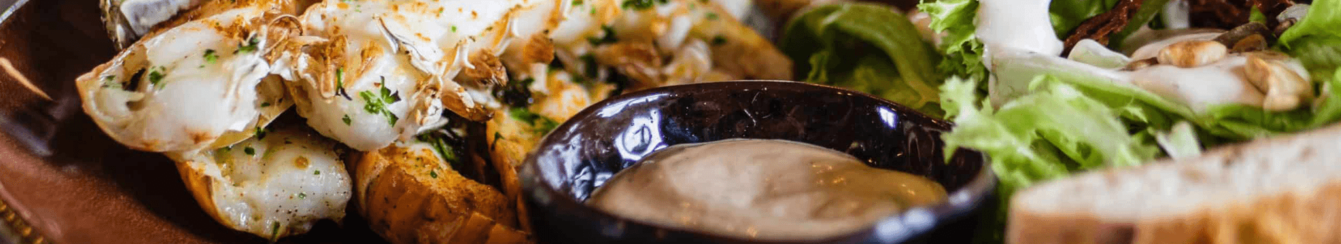 A plate of grilled seafood with a side of salad, dipping sauce, and bread.