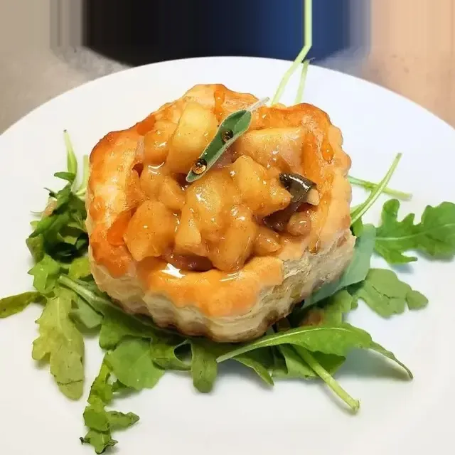 A pastry shell filled with savory apple and vegetable filling, garnished with greens on a plate.