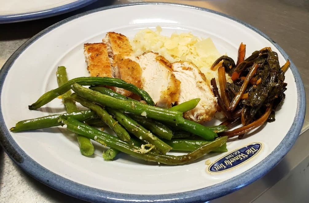 A plate of sliced fried chicken, green beans, sautéed greens, and mashed potatoes.