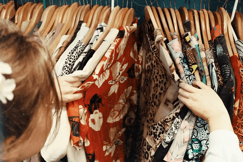 A person browses a colorful array of hanging clothing in a closet.